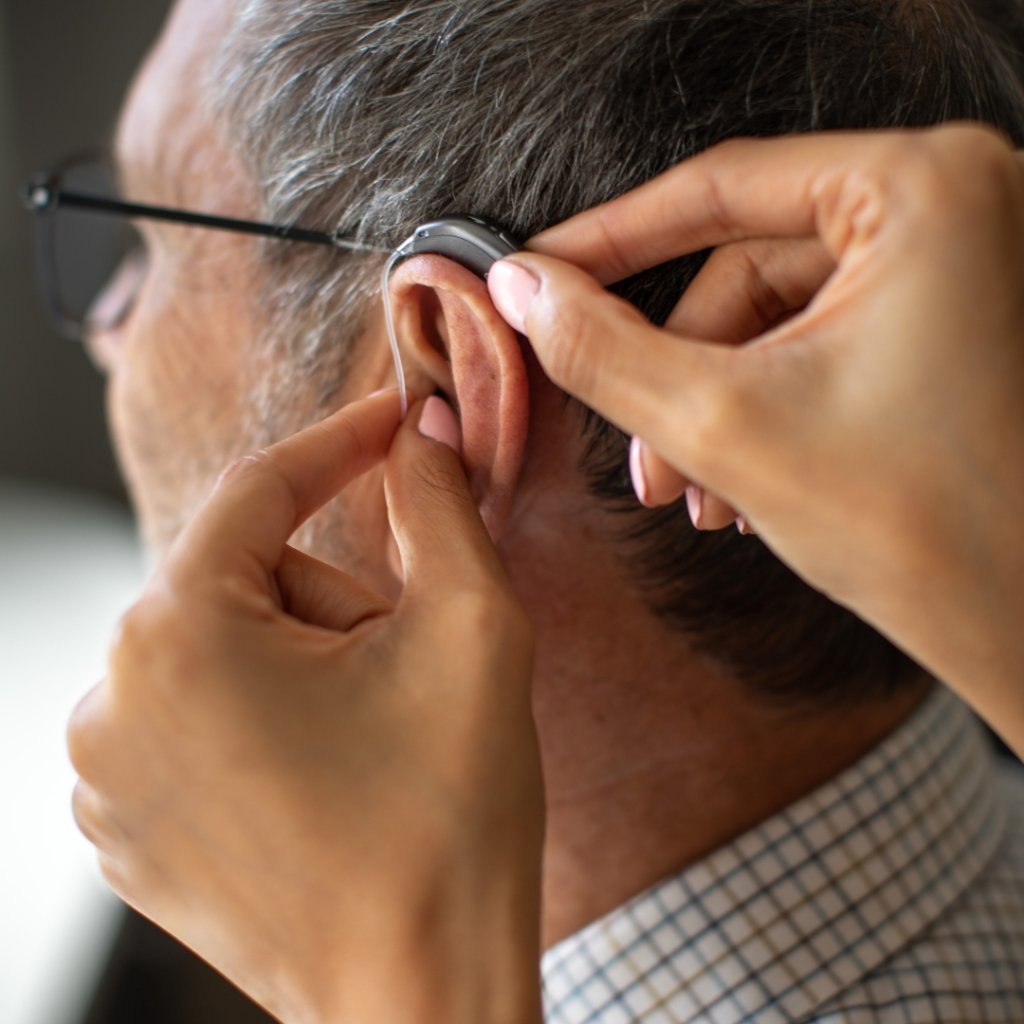 A person adjusting or inserting a hearing aid in an elderly man's ear.