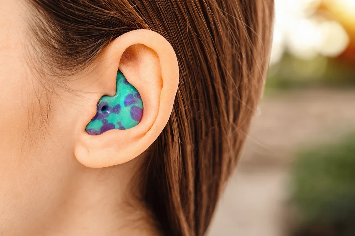 Close-up of a person's ear with a colorful, camouflage-patterned hearing aid in it.