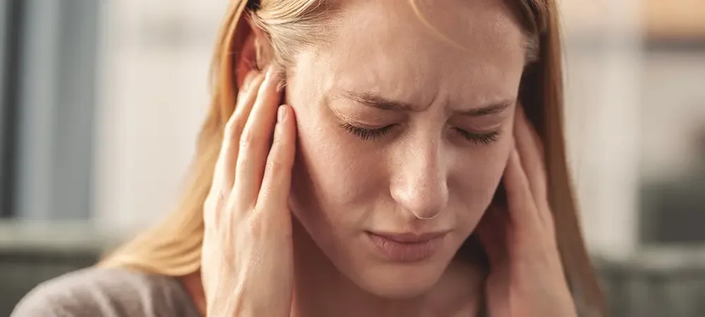 A woman experiencing a headache, pressing her fingers to her temples with a pained expression.