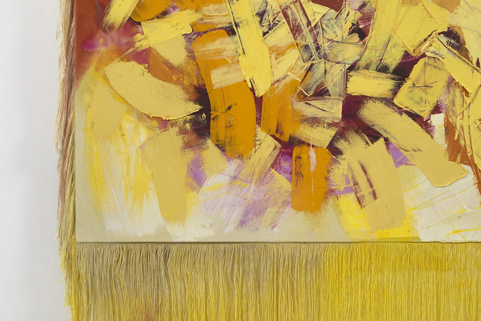 Close-up of an abstract painting with yellow, orange, and purple brushstrokes on a canvas with yellow fringe at the bottom.