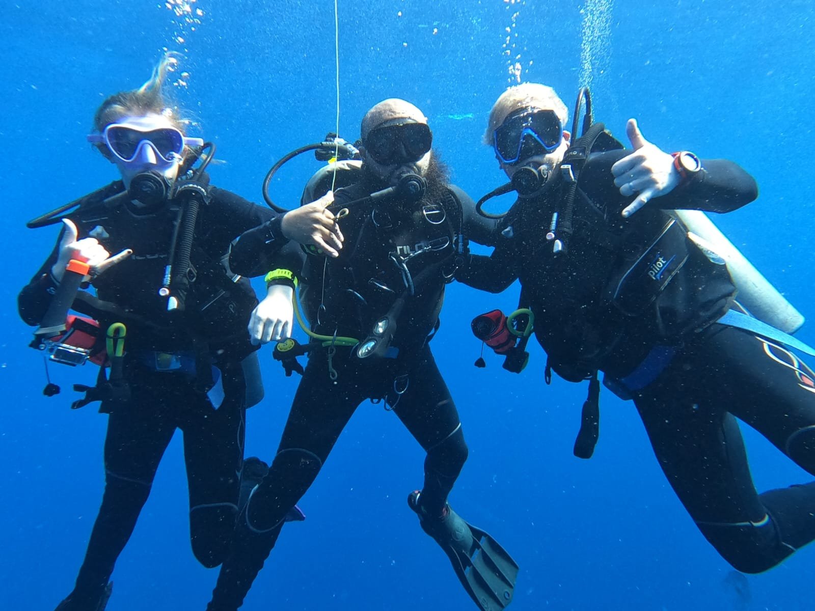 Tres buzos con equipo de buceo haciendo seña de signo de paz y saludo en el agua.