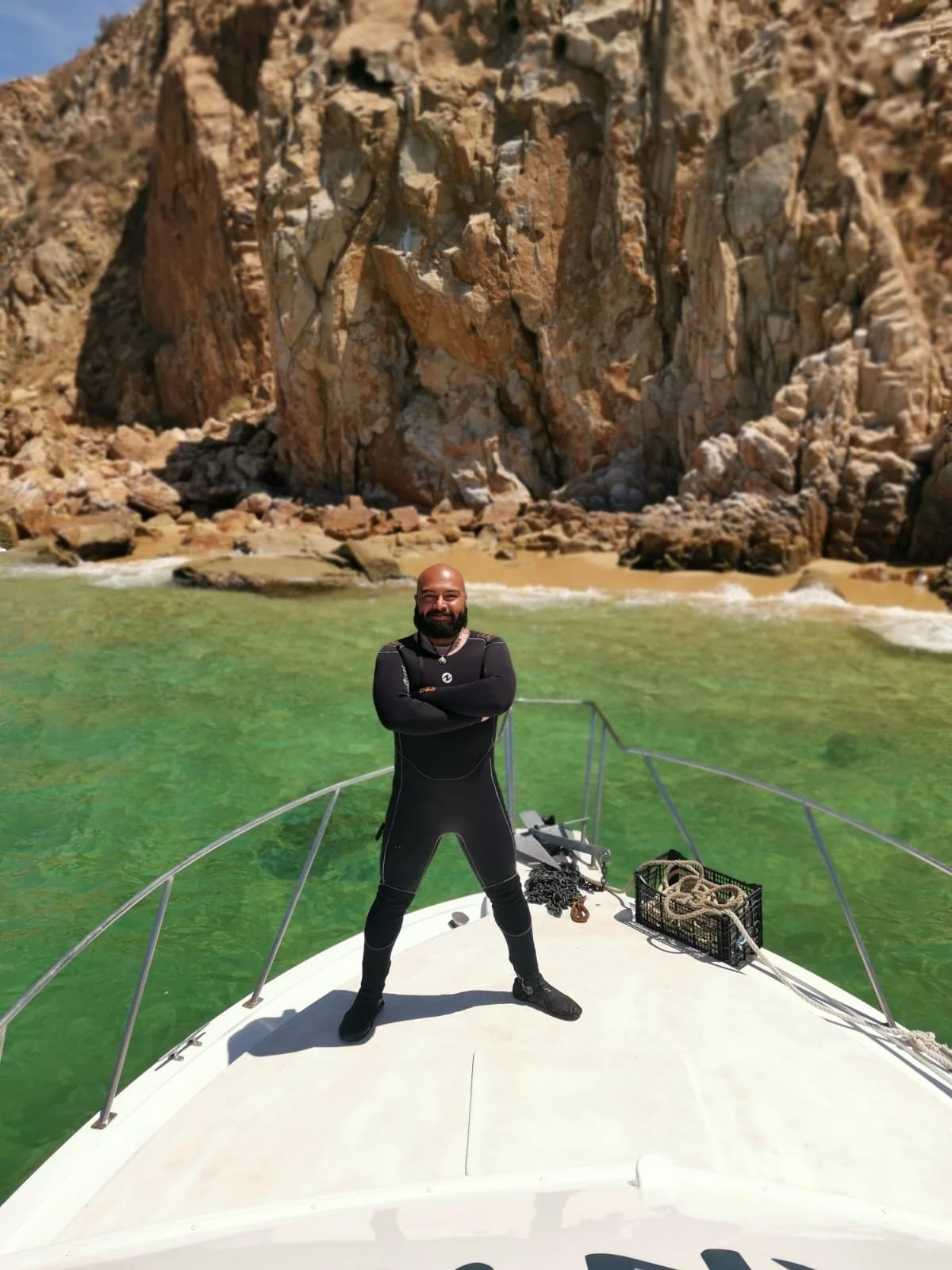 Hombre de pie en el proa de un barco con una roca y playa al fondo