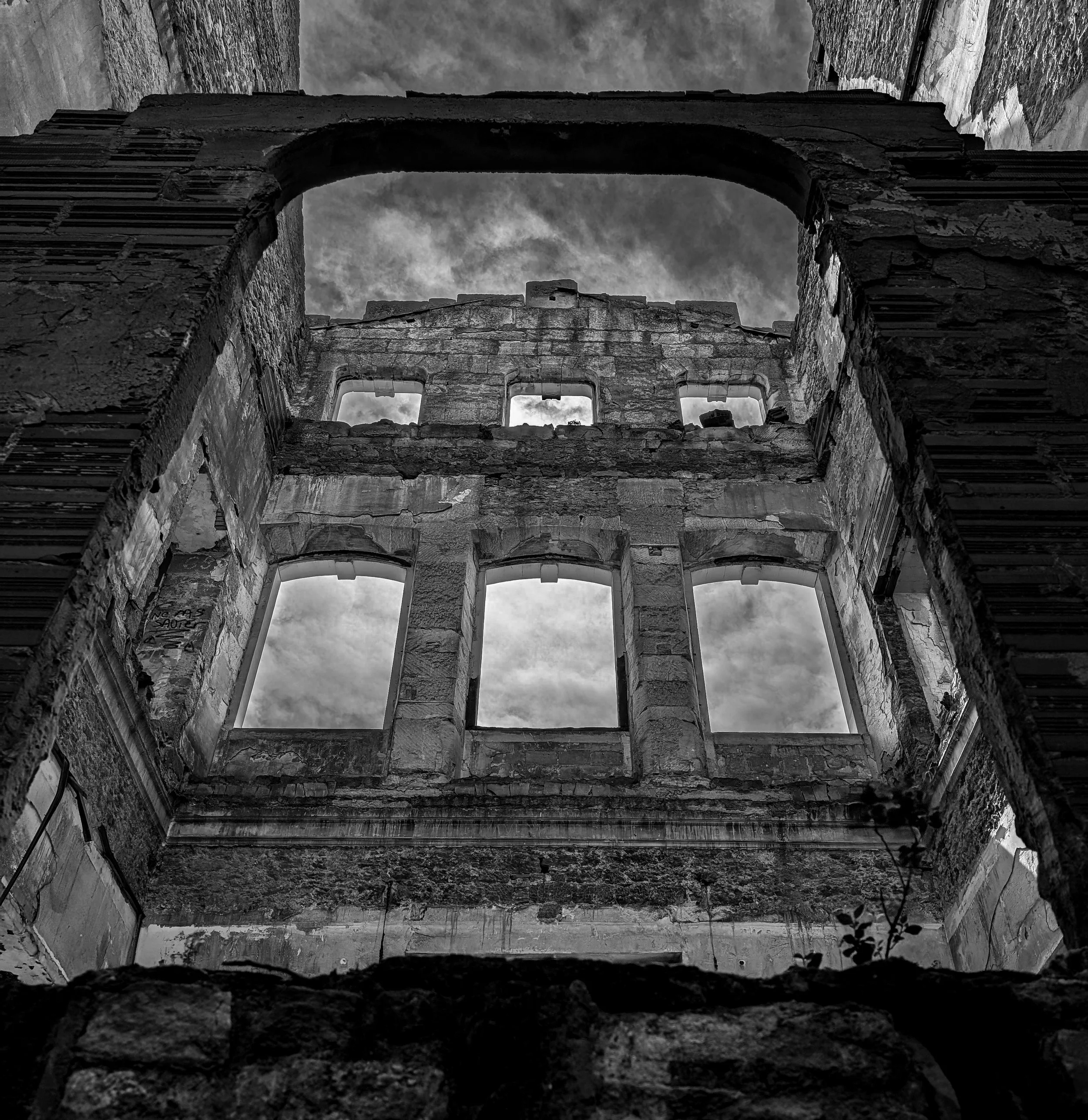 Black and white photo of the ruins of a building with sentinel windows, showing a cloudy sky through the empty window frames.