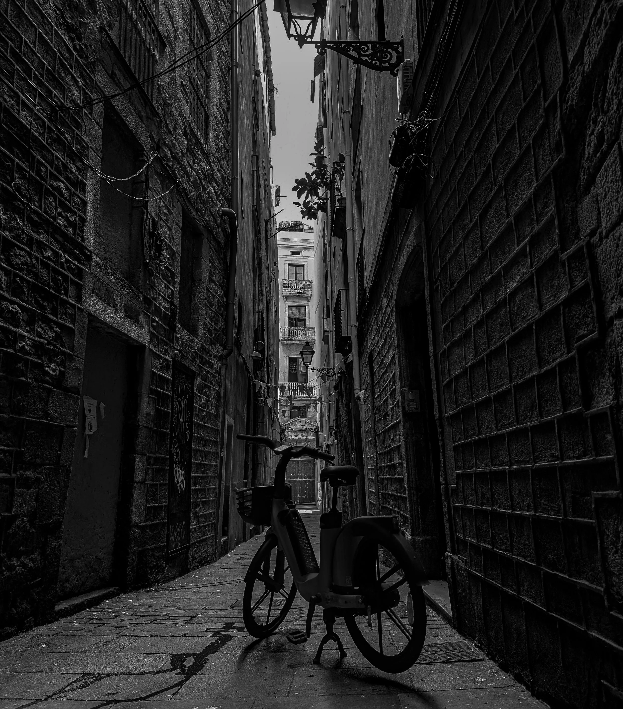 Black and white photo of a narrow alleyway with tall buildings on both sides and a bicycle in the foreground.