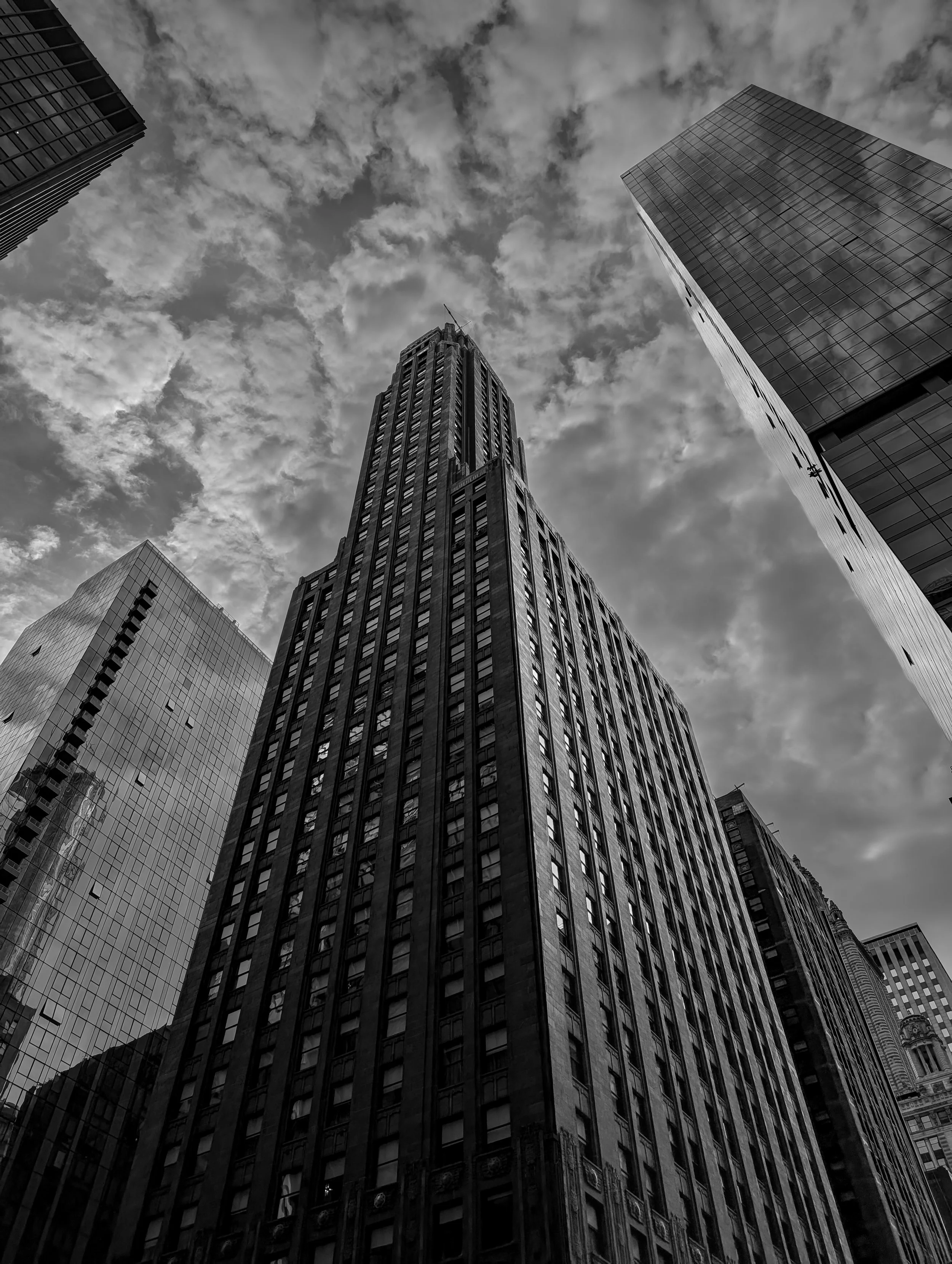 Black and white photo of tall skyscrapers viewed from the ground, with a cloudy sky overhead.