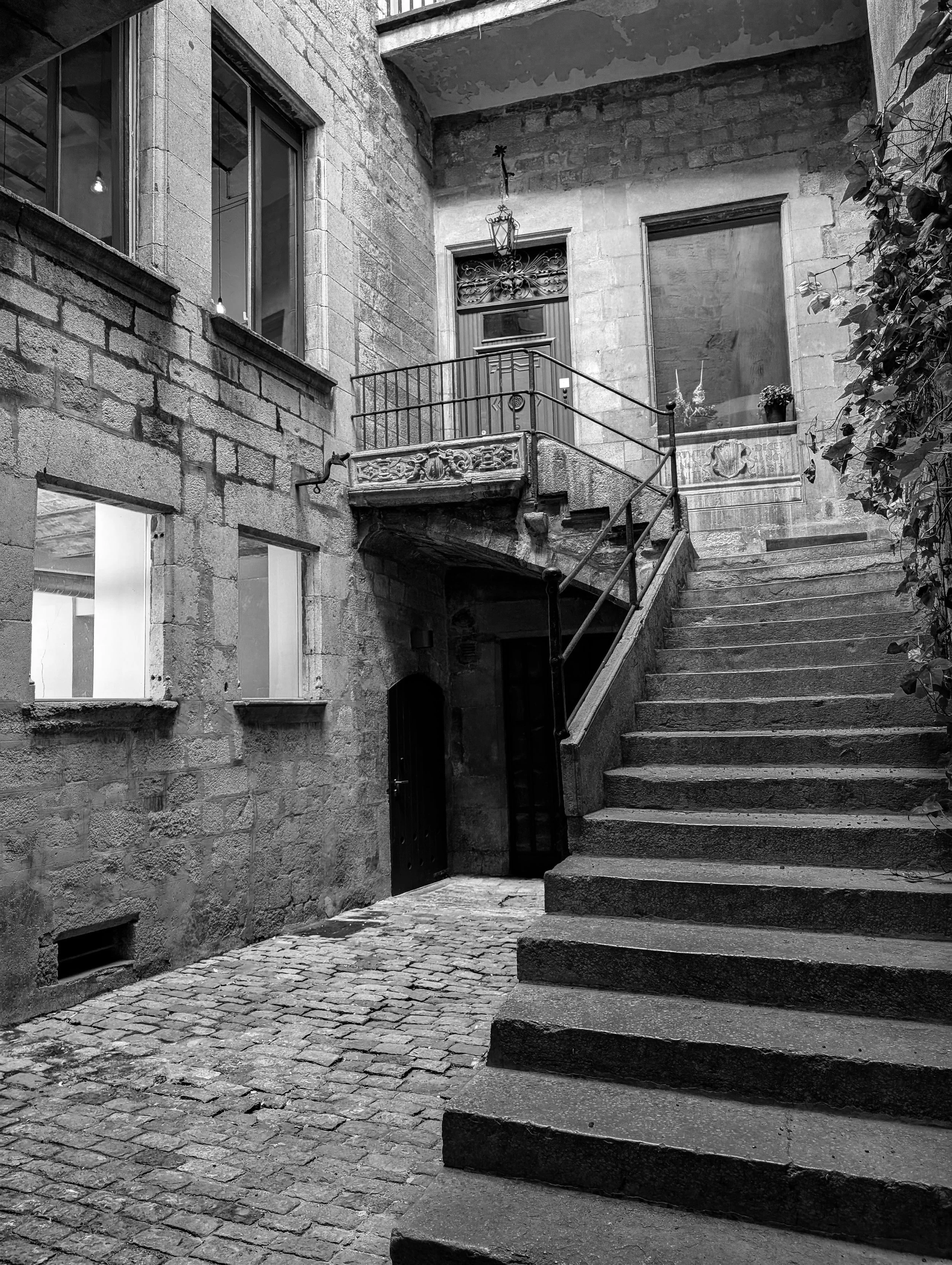 Black and white photograph of a stone stairway rising upward between textured walls, with light guiding the eye toward the top of the frame.