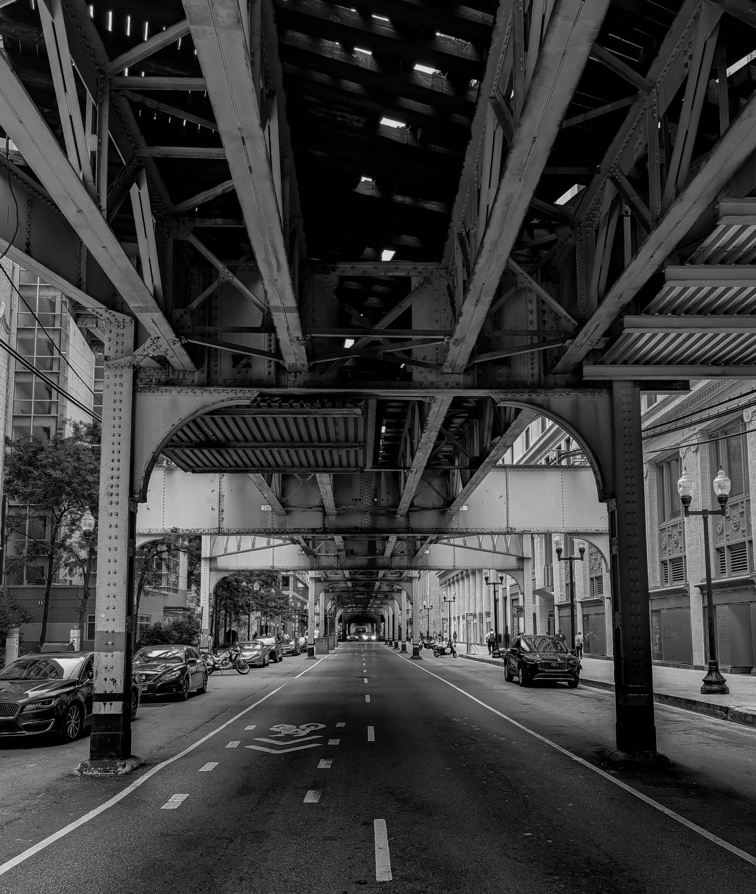Black and white image of structural beams and architectural elements forming intersecting lines and geometric patterns within an urban environment.