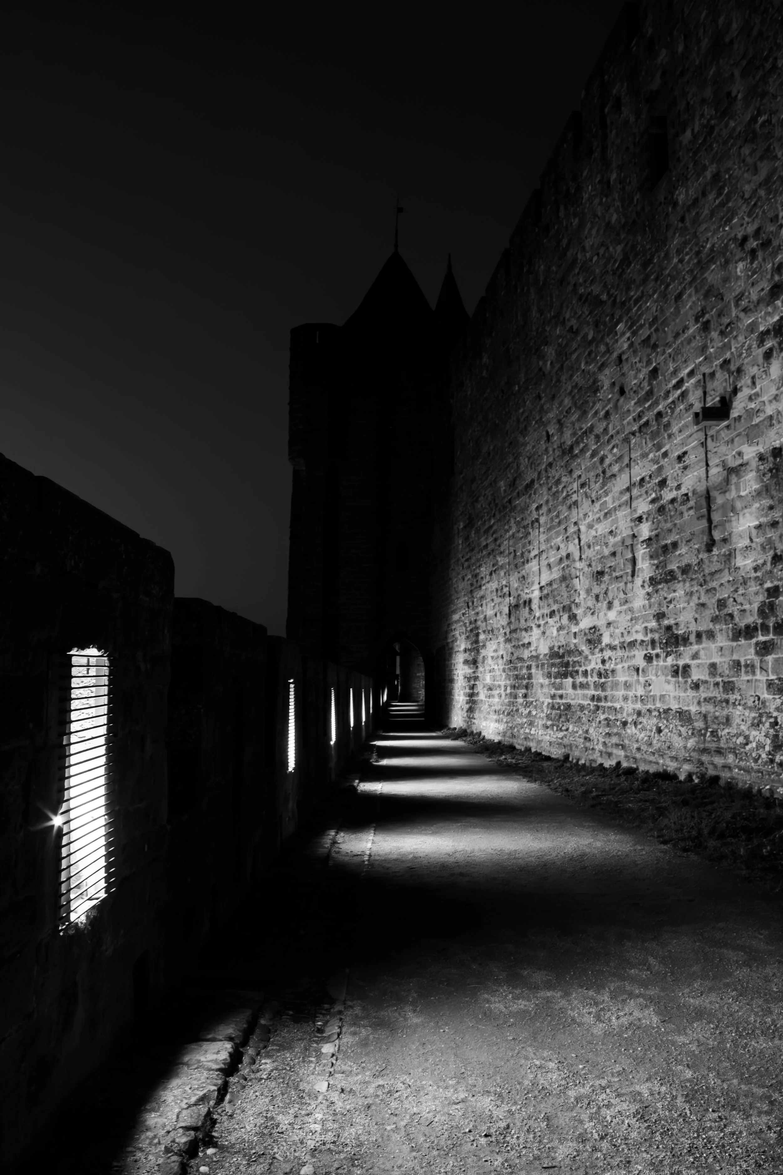 Black and white urban scene with soft light illuminating architectural surfaces, creating contrast between shadowed areas and glowing highlights.