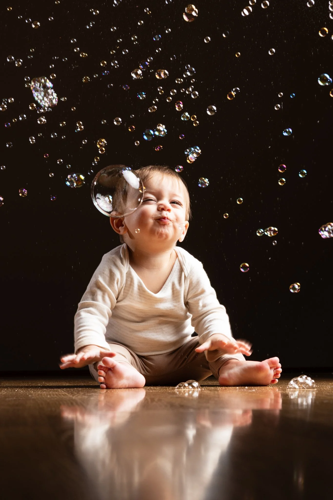 A young child sitting on the floor surrounded by floating soap bubbles, with a black background.