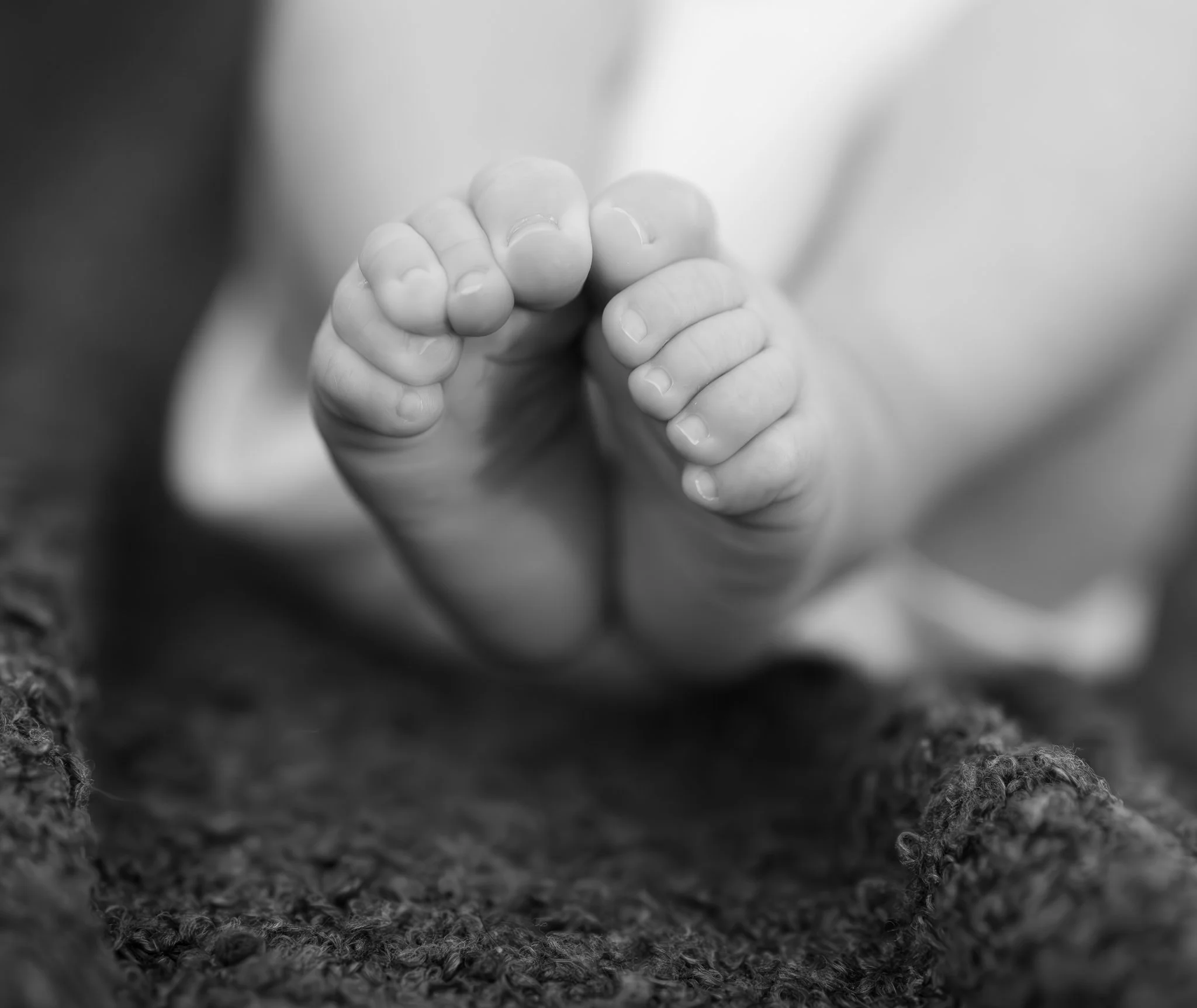 Close-up of a baby's tiny hand grasping an adult's finger, shot in black and white. Photographed from home in Braintree Essex Anne Wills Photography 