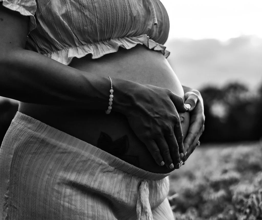 Close-up of a pregnant woman holding her belly with both hands outdoors, in black and white