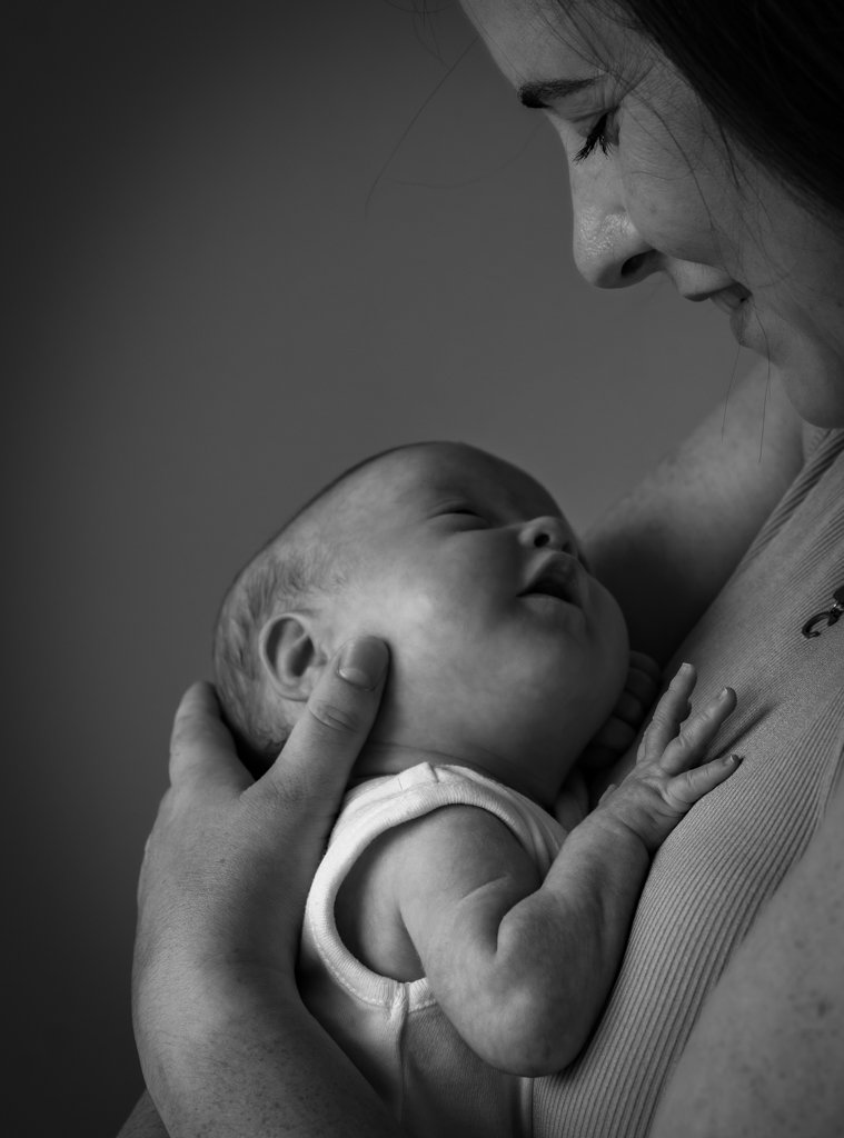 Black and white photo of a woman holding a sleeping baby close to her chest, smiling gently.