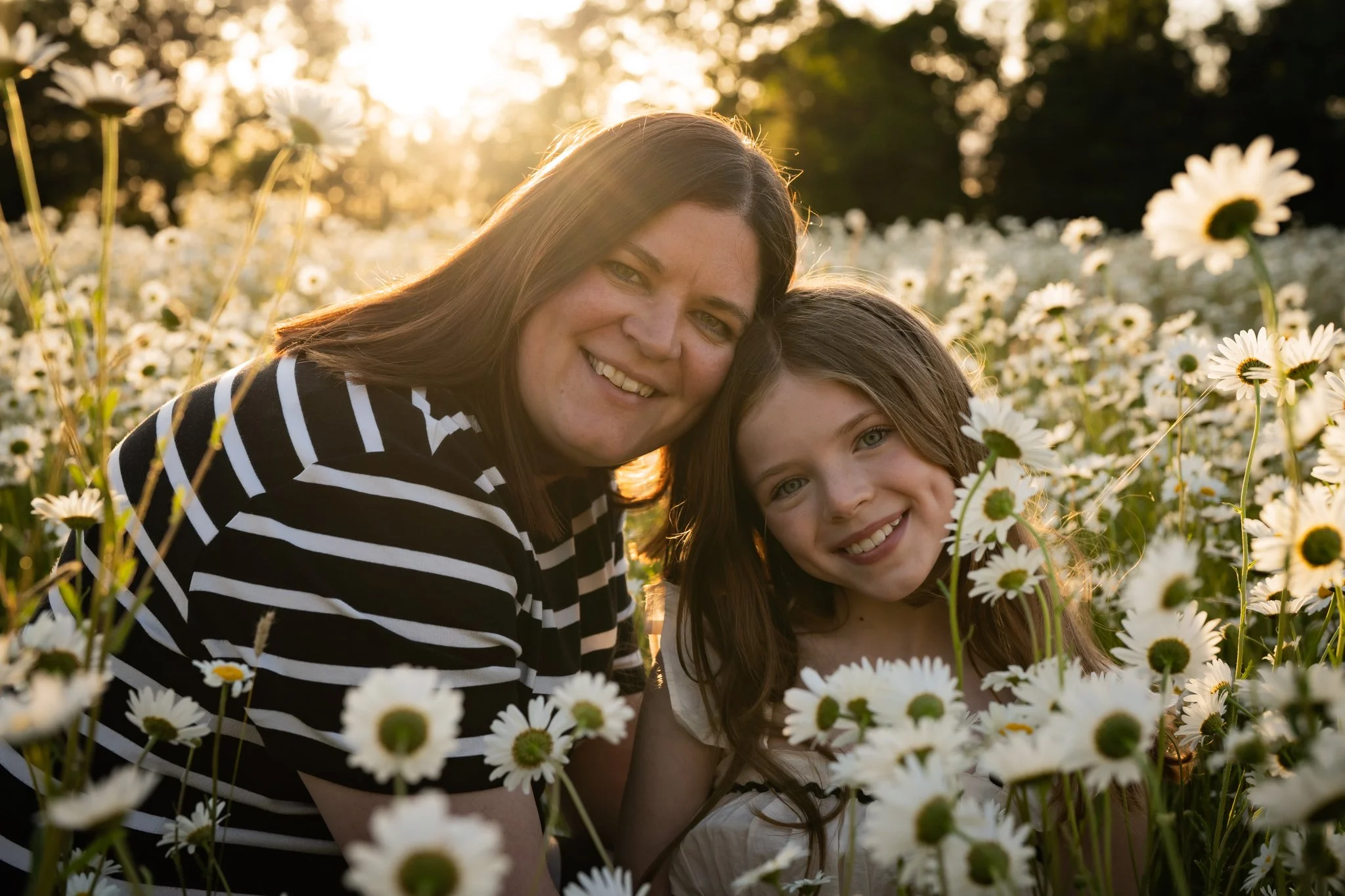 A woman and a girl smiling in a daisy field at sunset. Anne Wills Photography. Braintree, Essex