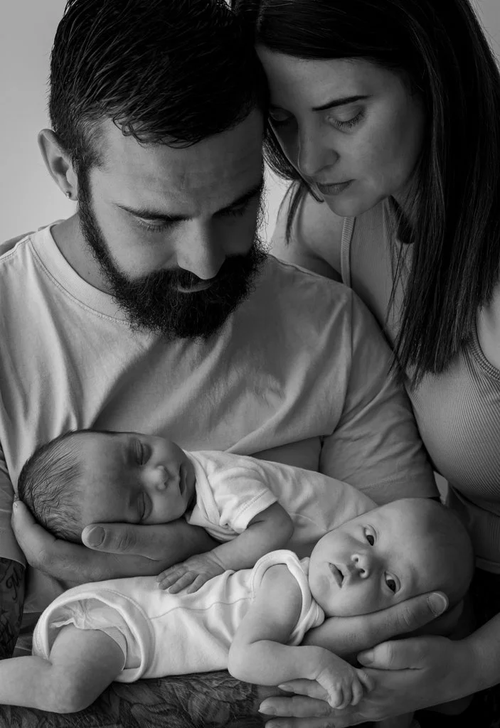 A black-and-white photo of a family with two infants being held by a man and woman, all looking at the babies with tender expressions.