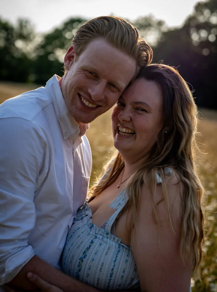 A happy couple smiling and hugging outdoors during sunset in a field. Anne Wills Photography. Braintree, Essex