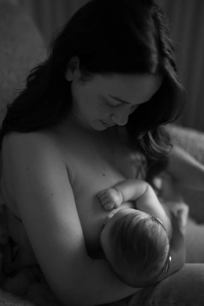 Black and white photo of a woman breastfeeding a baby, holding the baby close to her chest with her head bowed gently.
