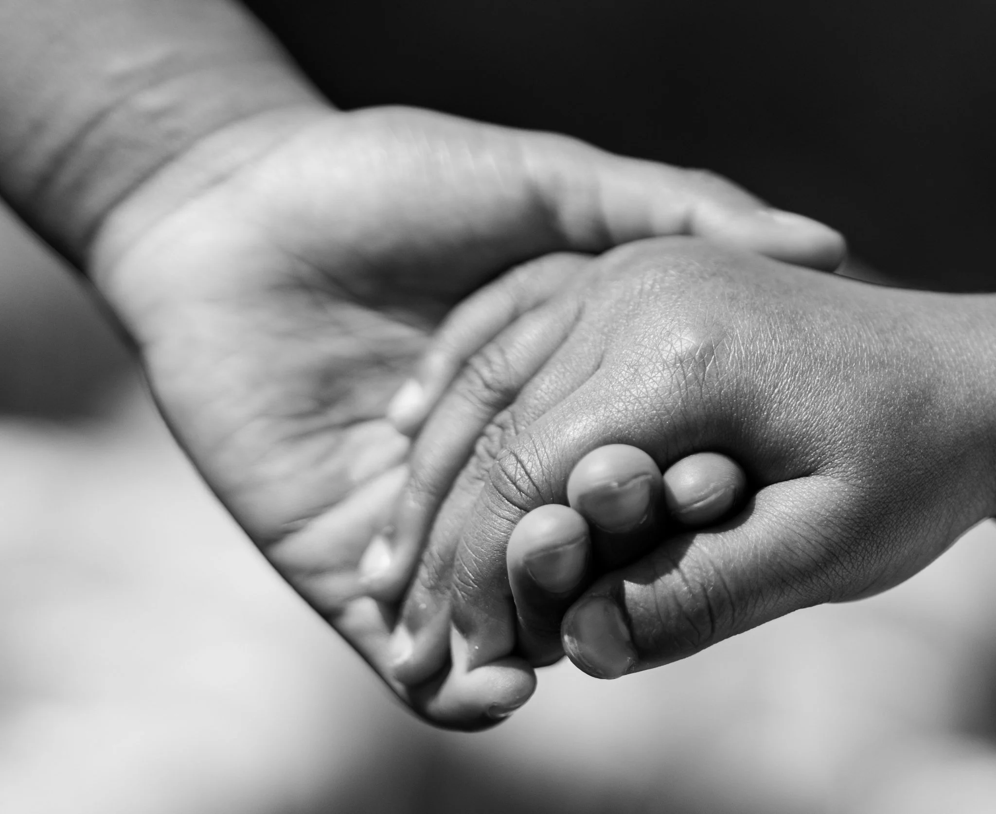 A black and white close-up of two hands clasped together, one with lighter skin and one with darker skin, symbolizing unity or connection.