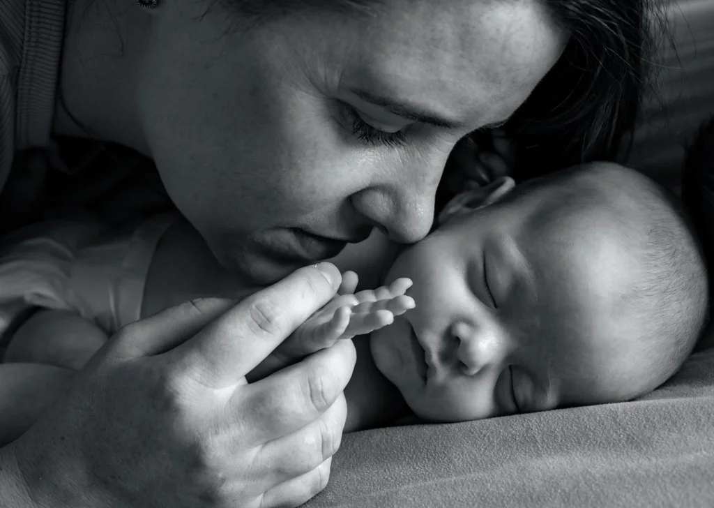 A woman lovingly holds and looks at a sleeping baby, touching its hand
