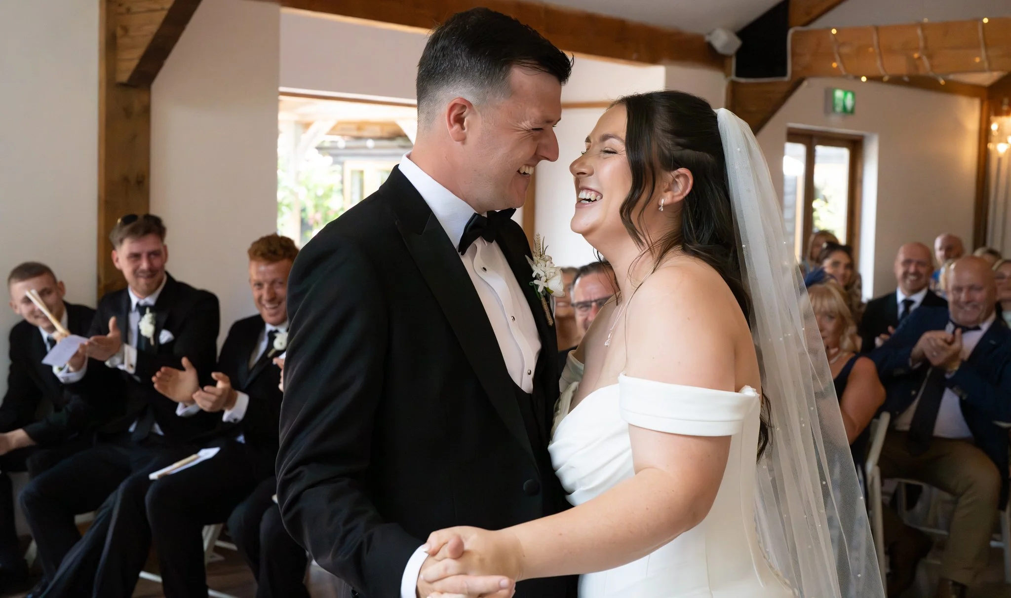 A bride and groom sharing a dance at their wedding ceremony, surrounded by smiling guests. Anne Wills Photography Maidens barn Essex