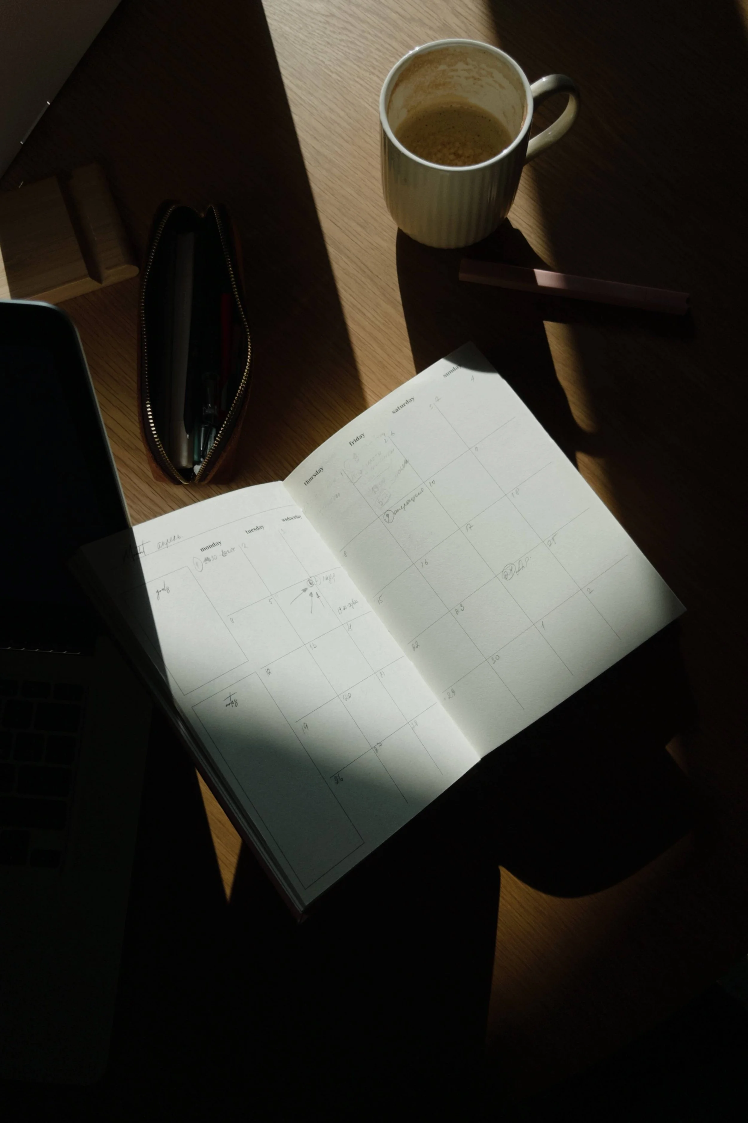 A desk with a cup of coffee, an open planner, a pen, and a laptop.