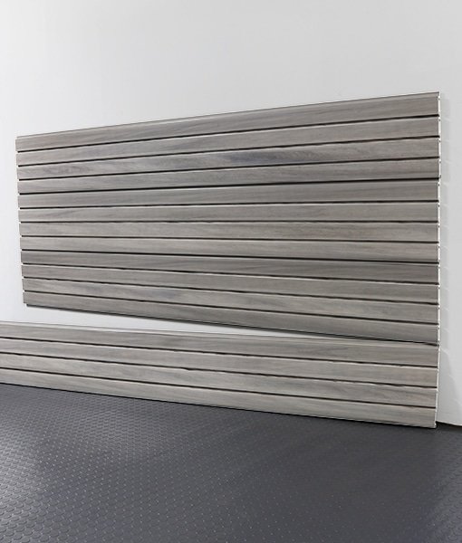 Two horizontal wooden slat panels leaning against a white wall in a room with dark dotted flooring.
