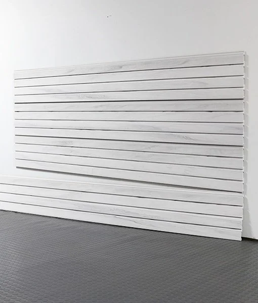 A white slatwall panel leaning against a white wall in a room with a gray textured floor.