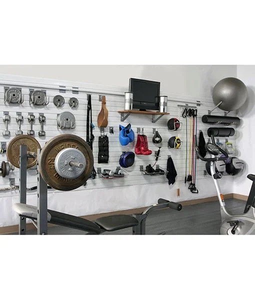 Home gym with weights, resistance bands, boxing gloves, and exercise equipment on a white wall with shelving.