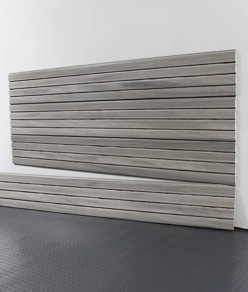 A large wooden slat wall panel leaning against a white wall on a dark textured floor.