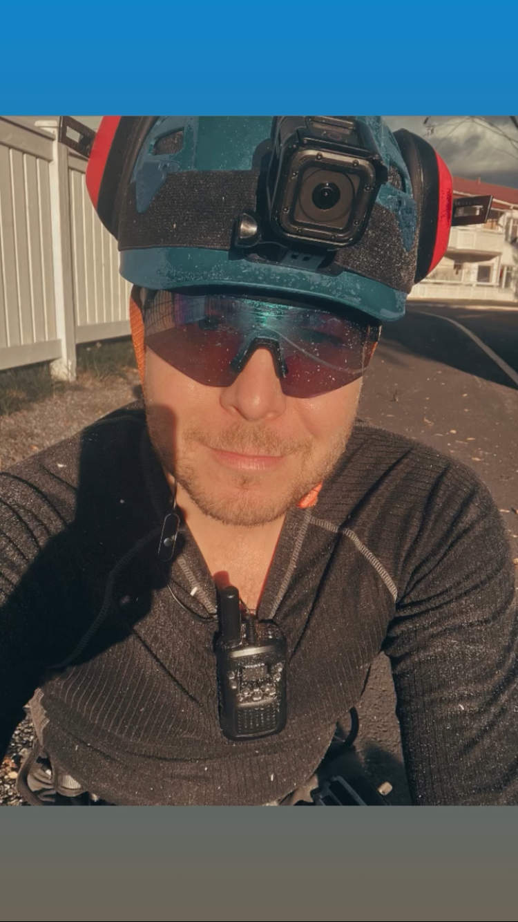 Person som tar selfie, bär hjälm med actionkamera, sportglasögon och sportkläder, utomhus på gata.