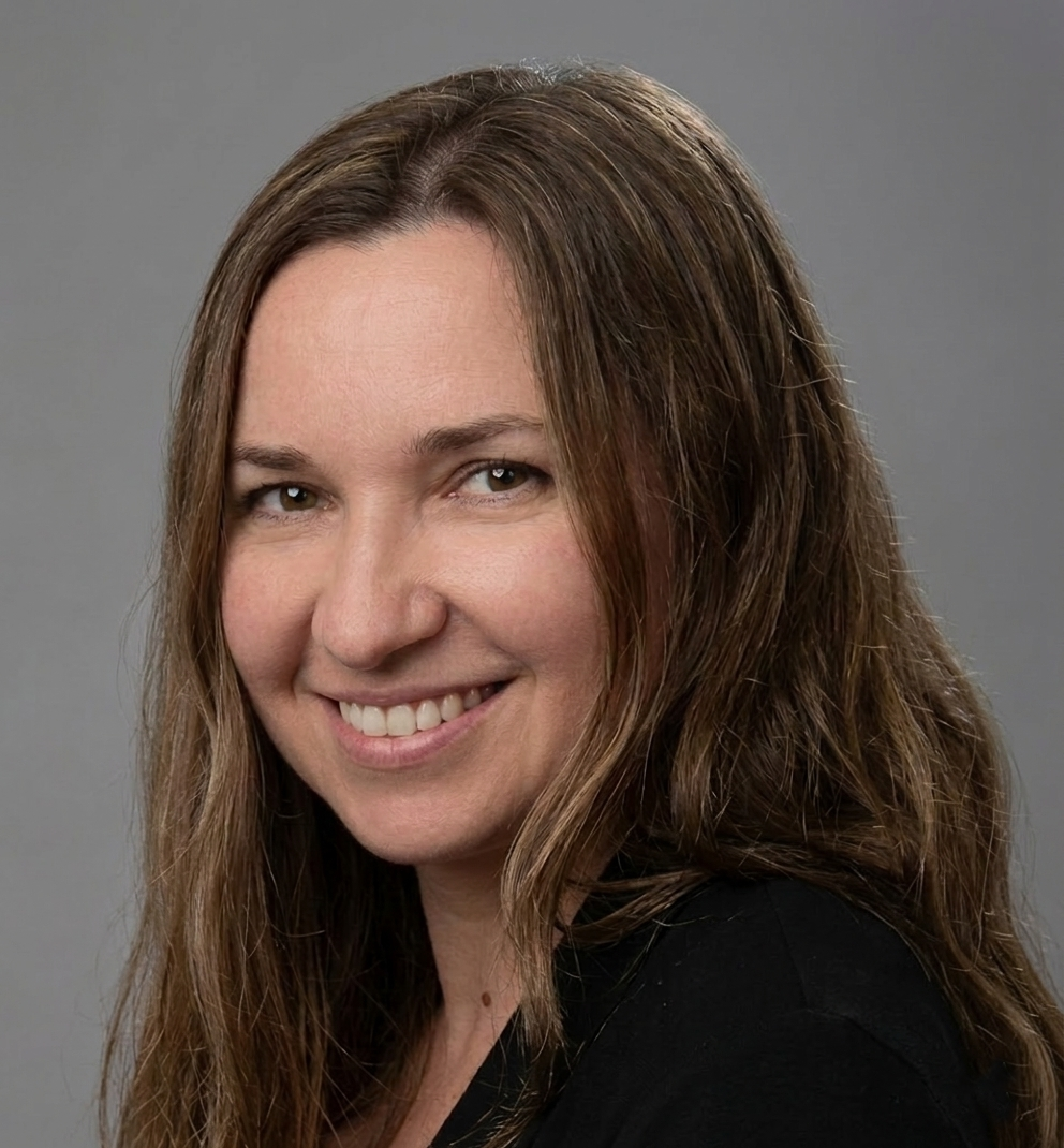 A woman with long brown hair smiling against a neutral grey background.