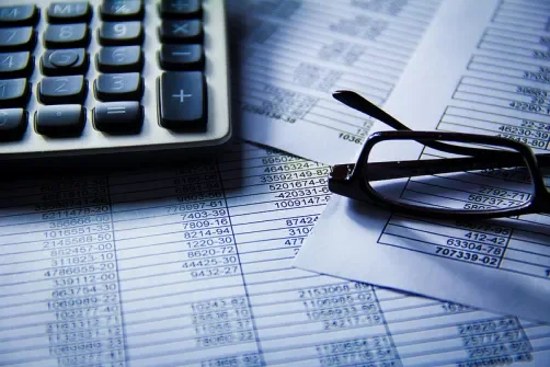 Financial documents with a calculator, eyeglasses, and a pen on top of printed spreadsheets.