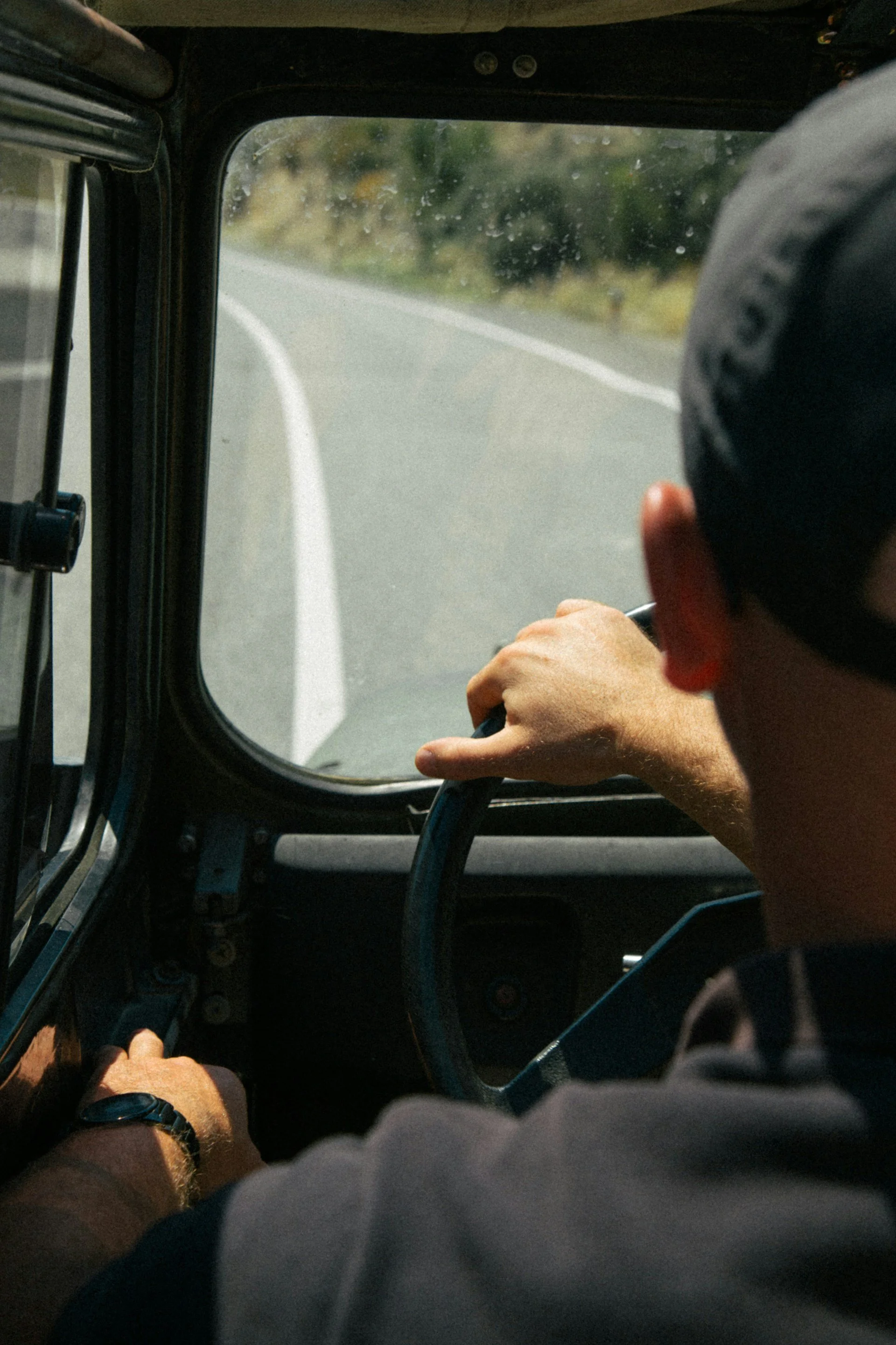 A person driving a vehicle on a winding road, wearing a watch and a cap.