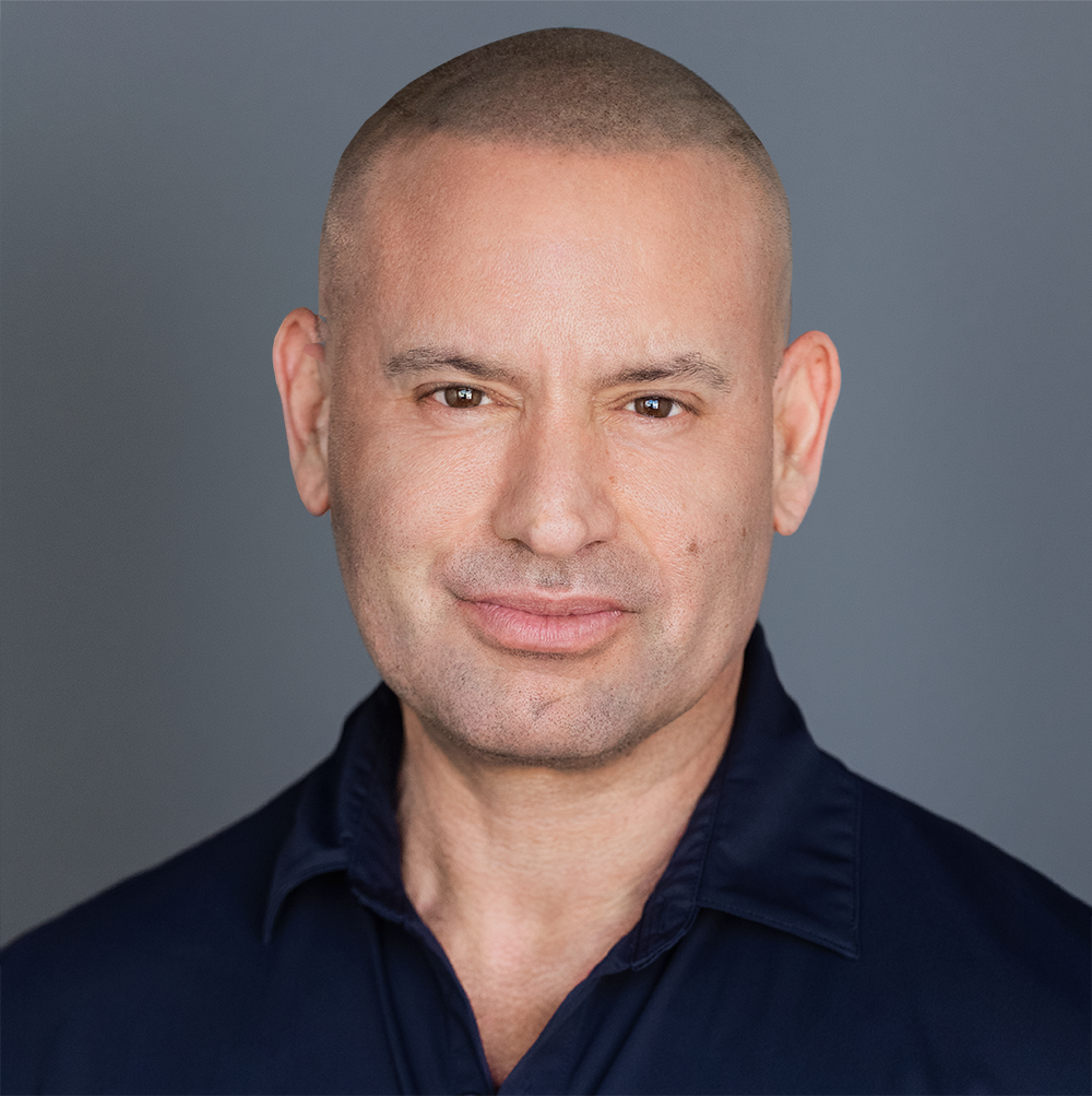 Headshot of a bald man wearing a dark shirt, smiling slightly, against a neutral gray background.