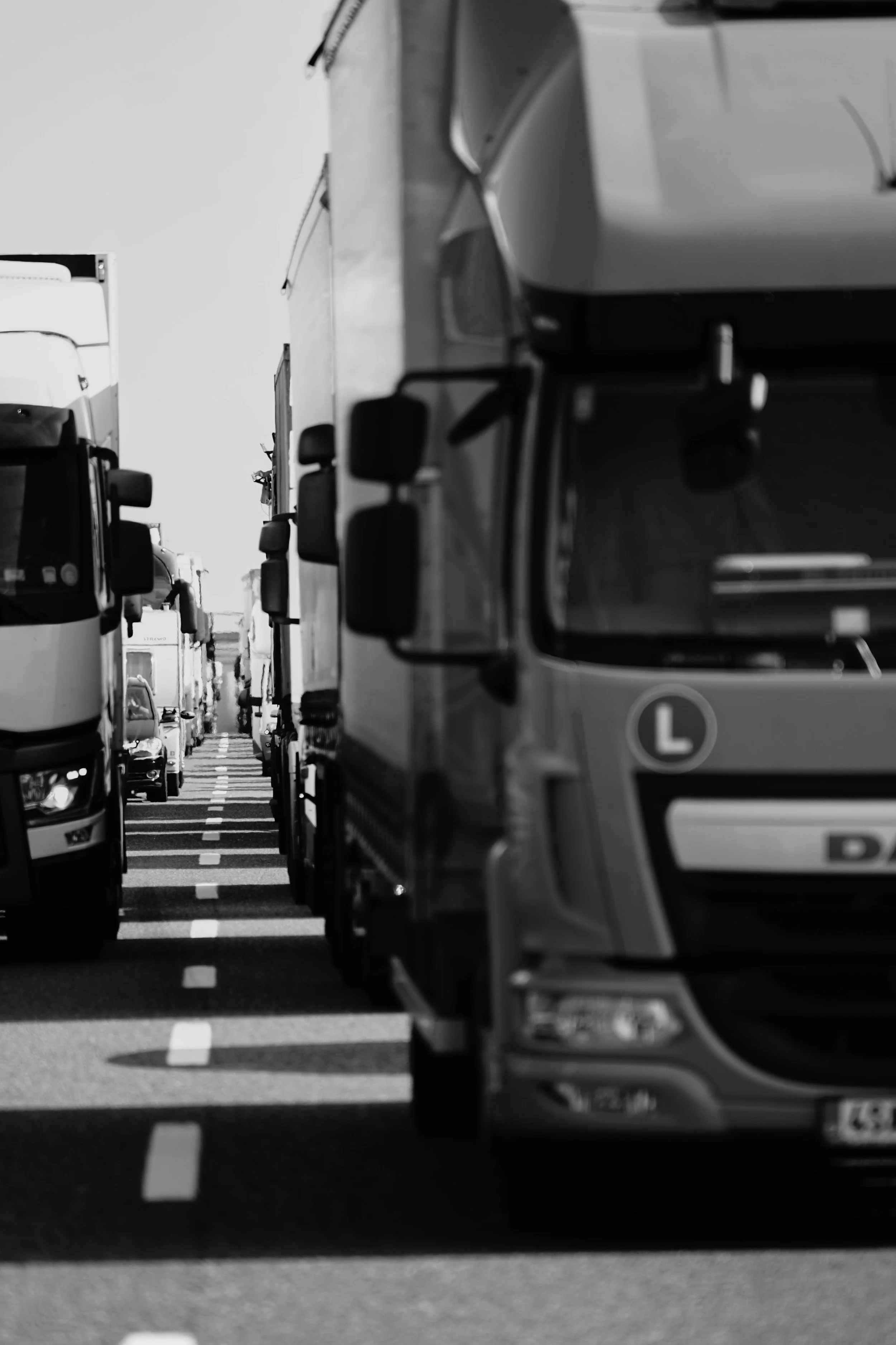 Black and white photo of multiple trucks parked closely on a roadway with dashed lane lines.