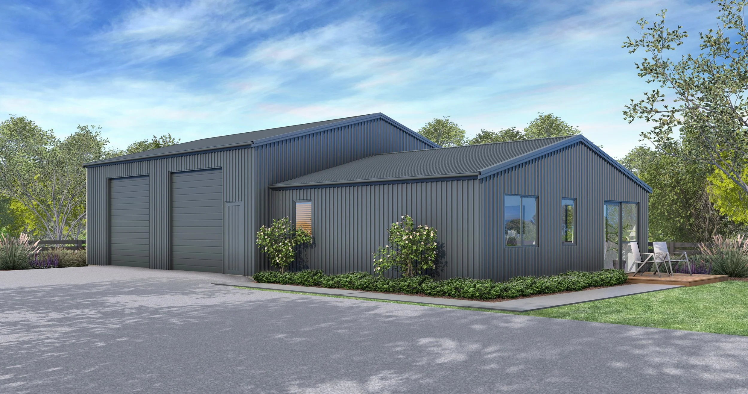 A modern gray metal building with a large garage door, a small window, and a patio with two chairs, surrounded by landscaped bushes and trees against a blue sky with clouds.