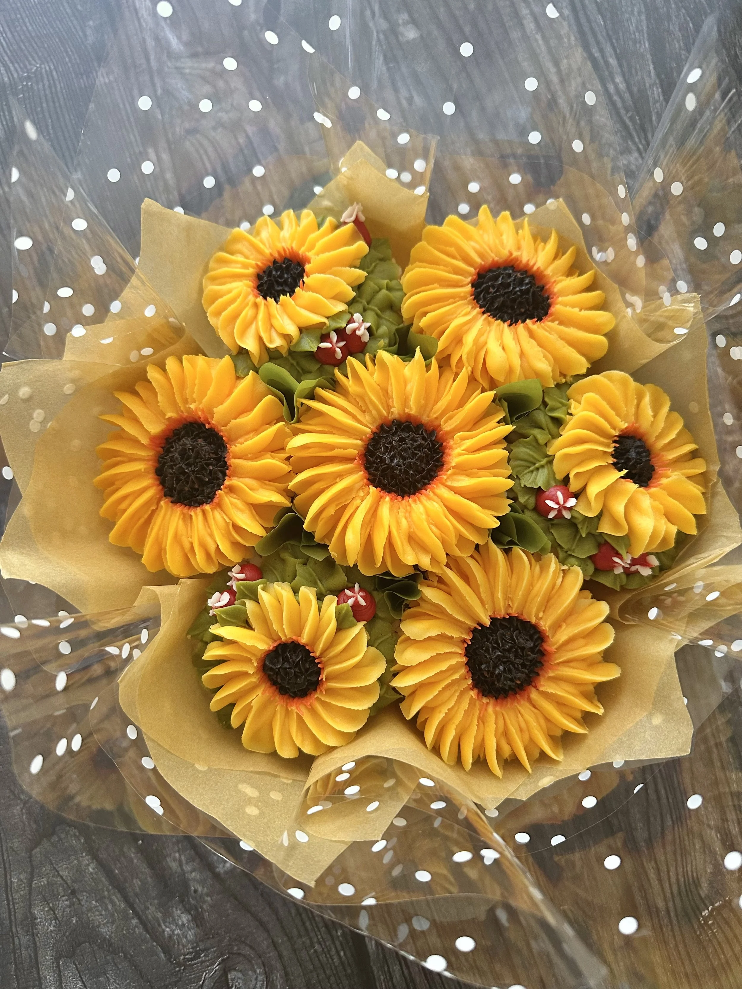 Bouquet of sunflower-shaped flowers wrapped in transparent paper with white polka dots, on a dark wooden surface.