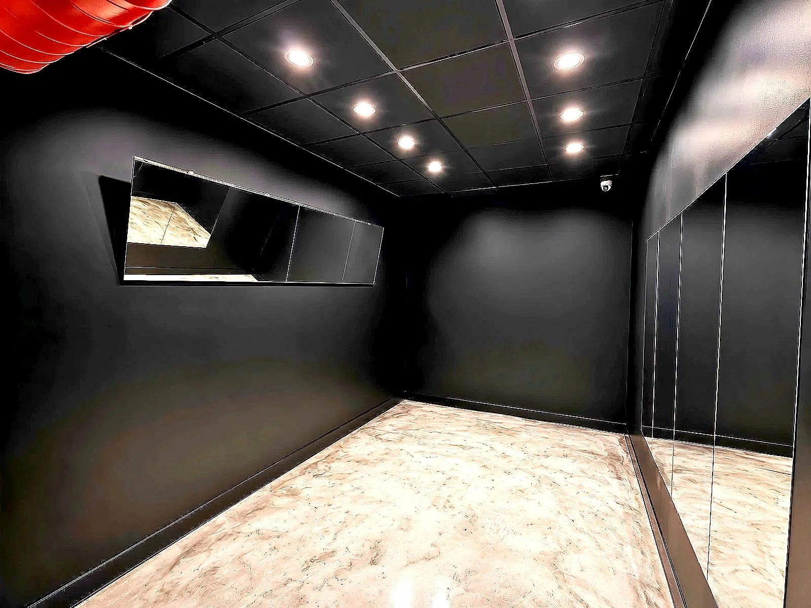 A posing room interior with black walls, a marble floor, and a mirrored wall with several doors. The ceiling has black tiles with recessed lighting.