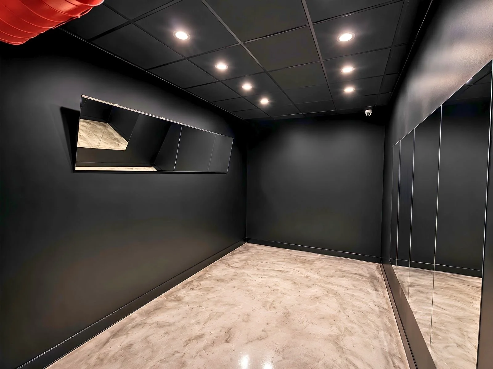 Empty black elevator interior with black walls, ceiling, and mirrored panels on the right side, beige marble flooring, and ceiling lights.