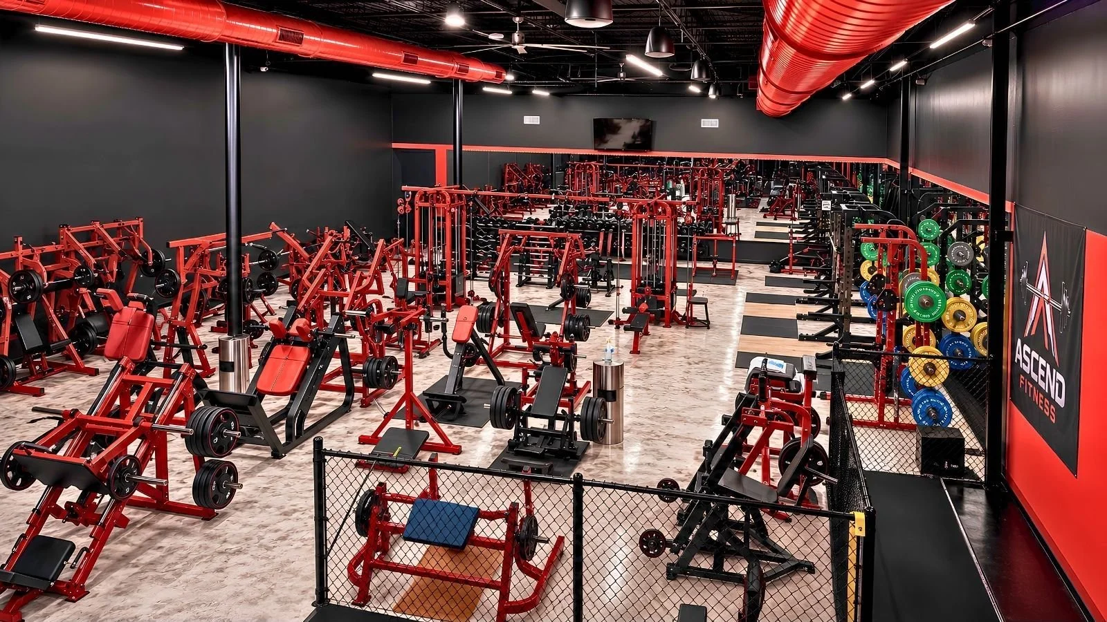 Interior view of a modern gym with red, black, and colorful weightlifting equipment and a mirrored wall.