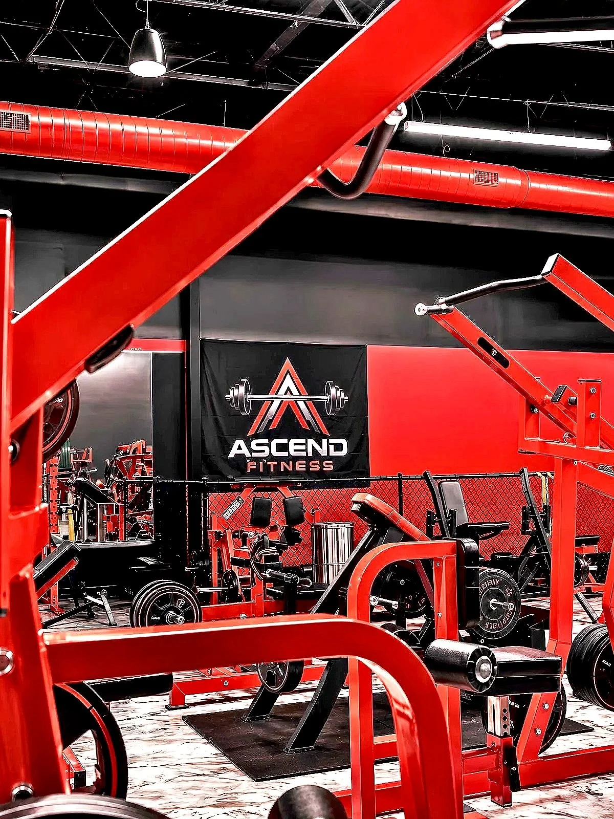 Interior view of Ascend Fitness Cypress with red fitness equipment, including weight machines, free weights, and a bench.
