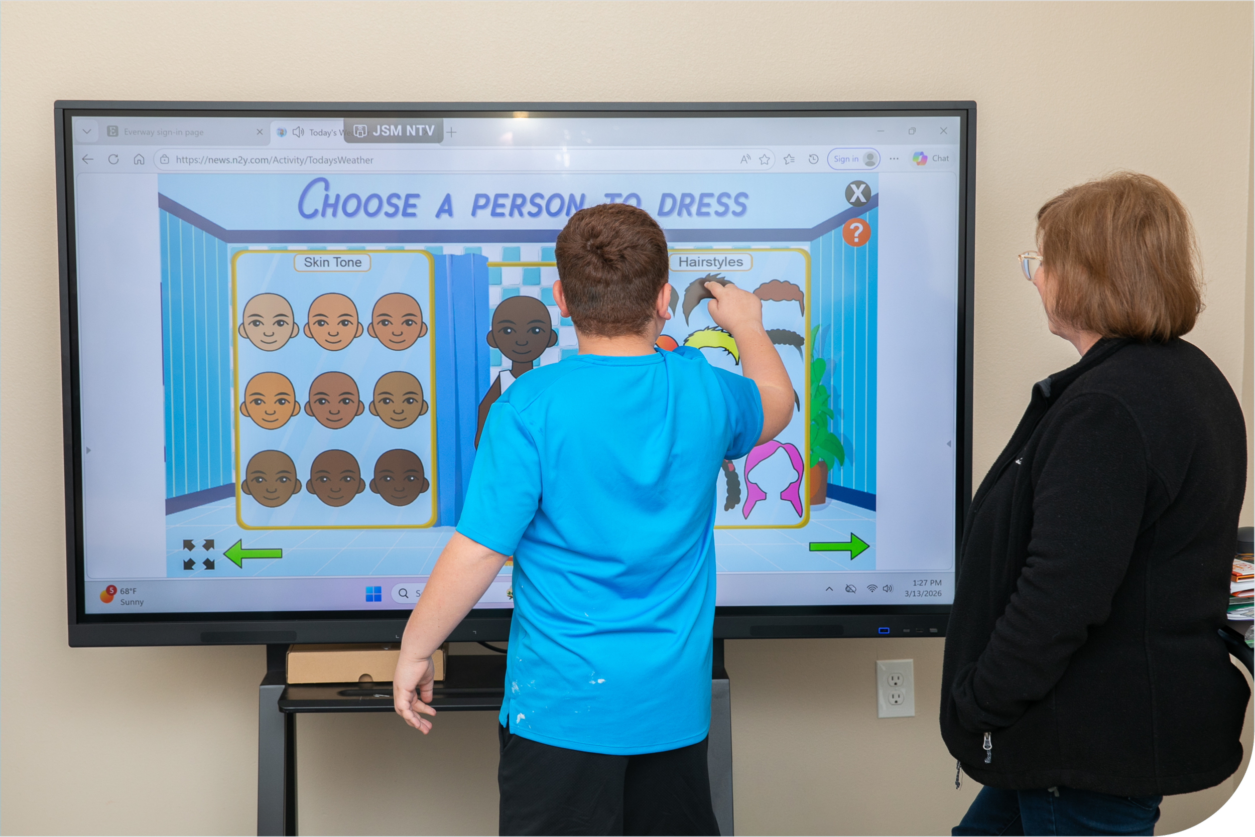 Child and adult standing in front of an interactive screen selecting a hairstyle and skin tone for a virtual avatar.