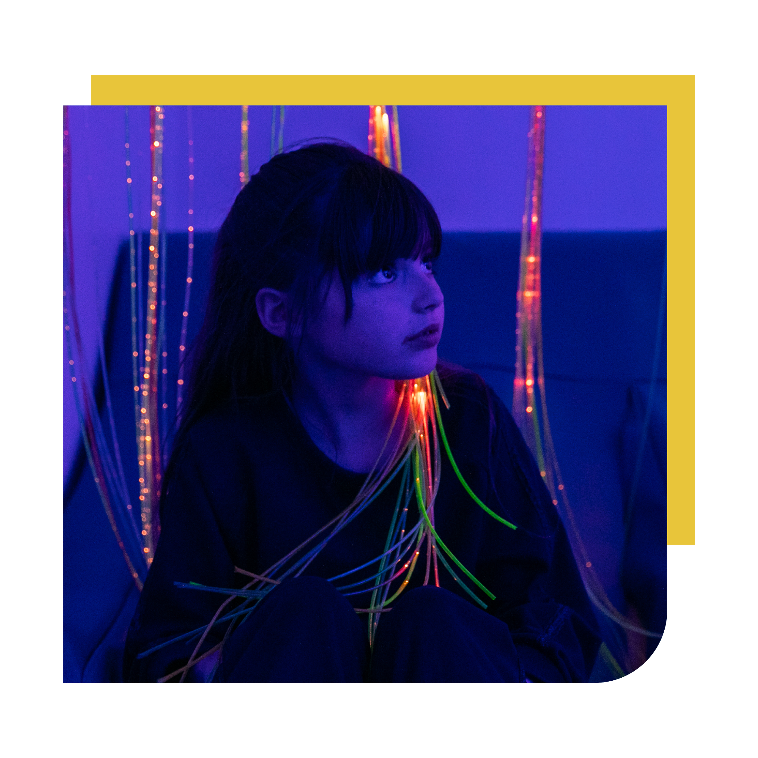 A person with long dark hair looking to the right, illuminated by purple and blue neon lights with hanging colorful string lights in the background.