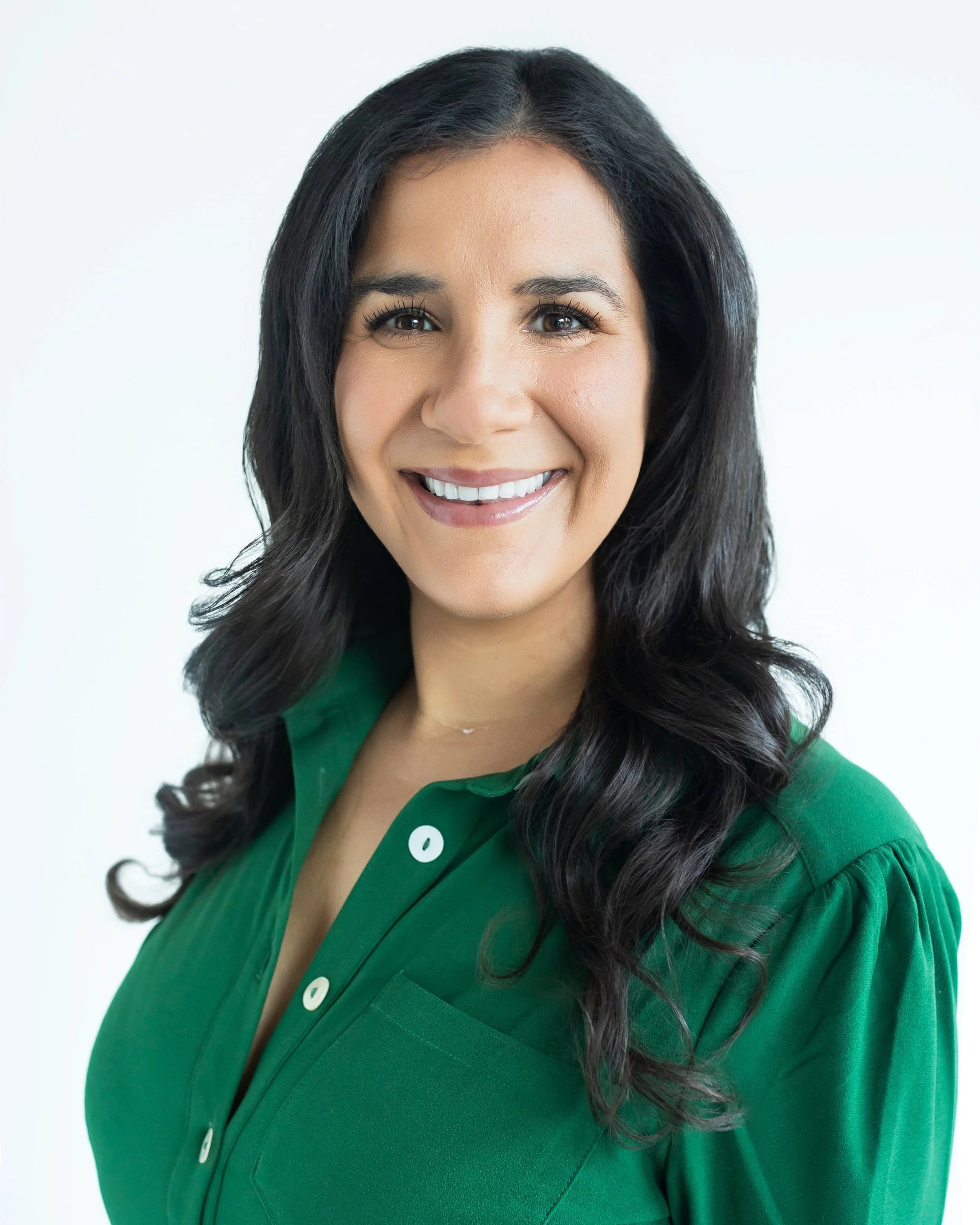 A woman with long dark hair, smiling, wearing a green button-up shirt, against a plain white background.