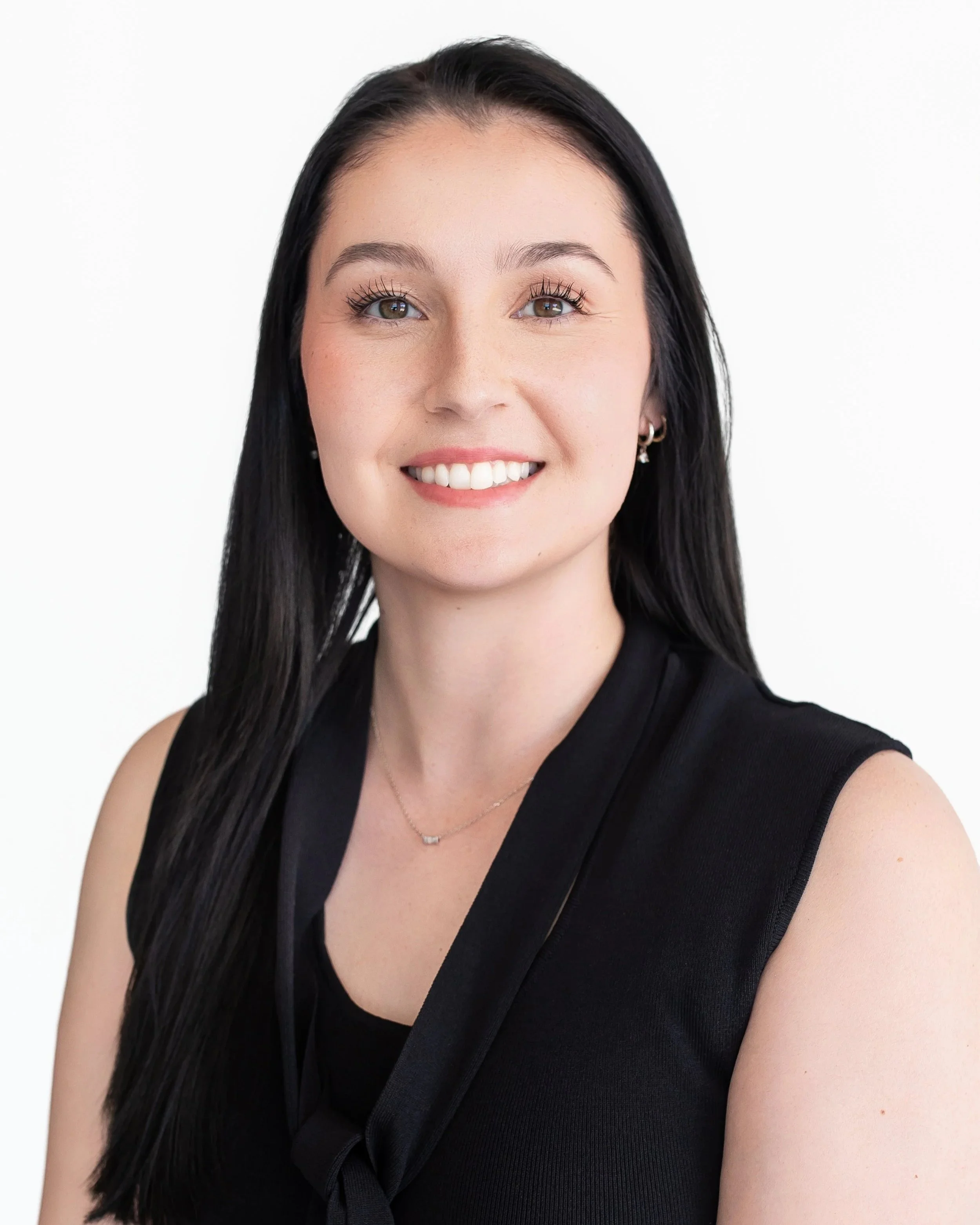 Young woman with long black hair, wearing a black sleeveless top, smiling, against a white background.