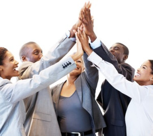 Five diverse businesspeople in formal attire giving each other a high-five, smiling.