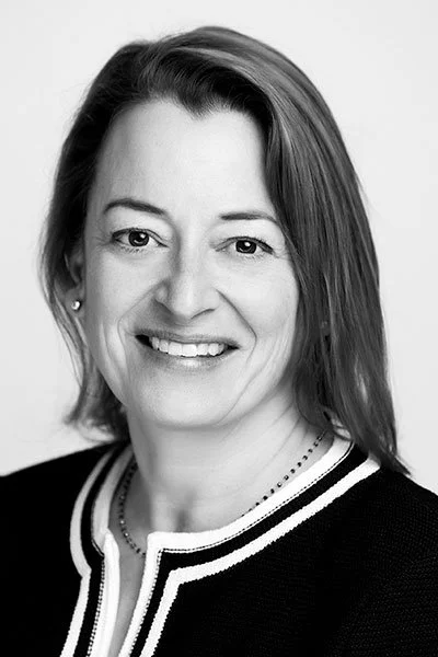 Black and white portrait of a smiling woman with shoulder-length hair, wearing a dark top with a striped collar.