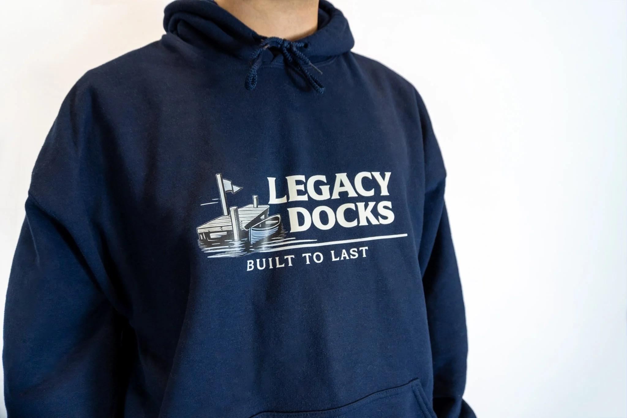 A person wearing a navy blue hoodie with a logo that reads 'Legacy Docks' and the tagline 'Built to Last'. The logo includes an illustration of a dock with a boat and a flag.