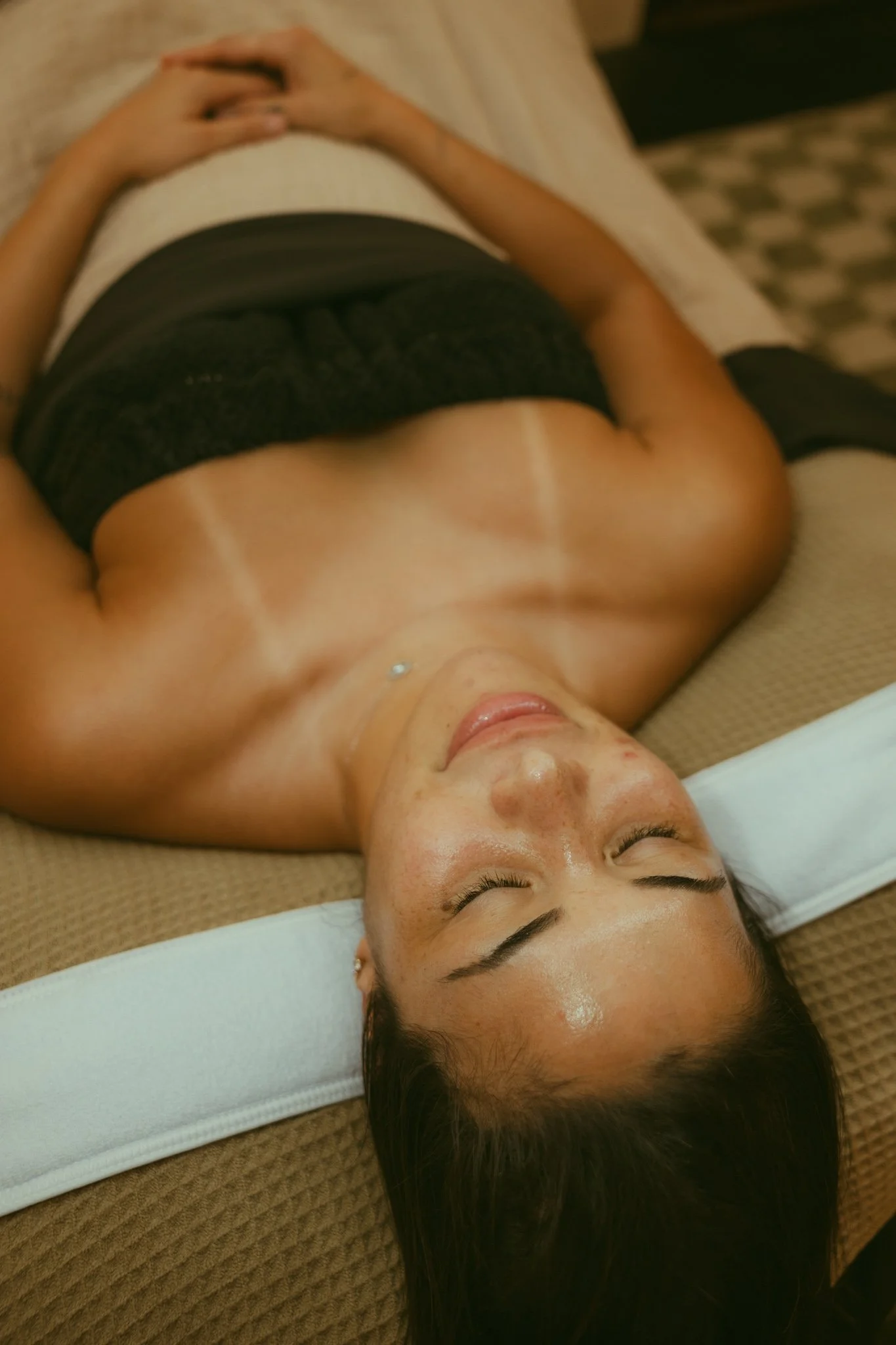 A woman lying on a massage table with her eyes closed, hair spread out, in a relaxed state during a massage or spa treatment.