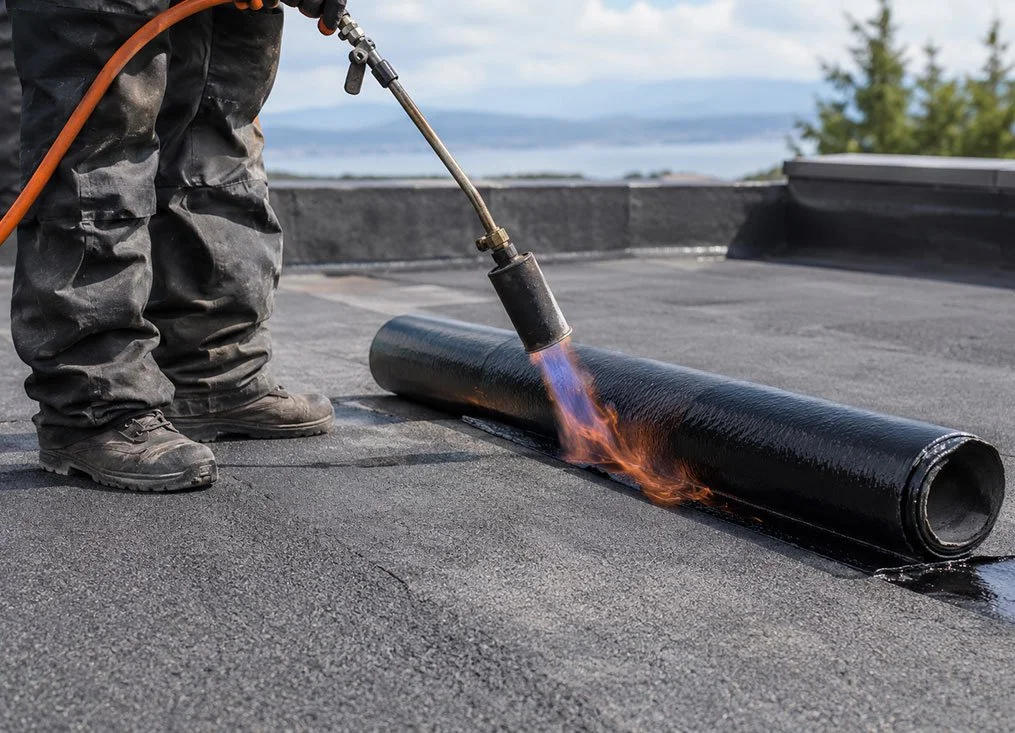 Worker applying a torch to seal a rolled roofing membrane.