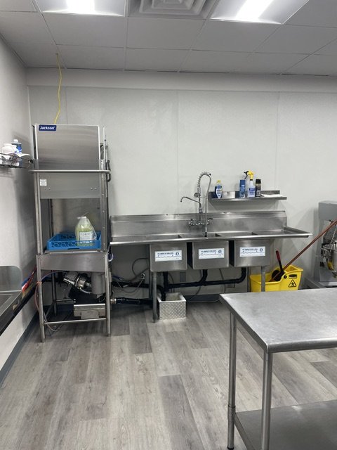 Commercial kitchen sink with cleaning supplies and mop placed nearby